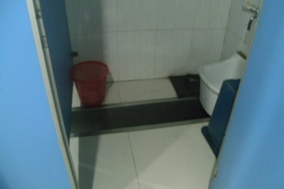 Squat toilet stall in China with a waste container beside the pan