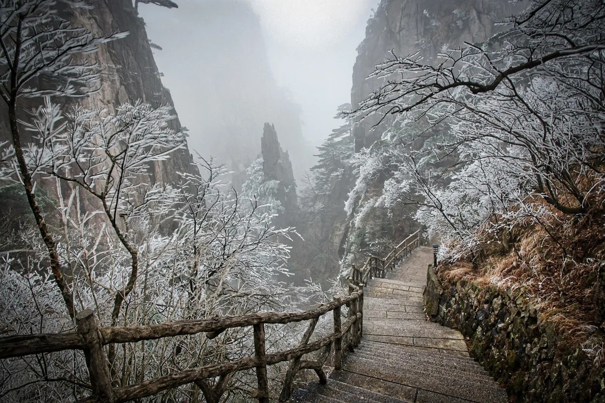 Snow-covered stone path between misty Huangshan peaks
