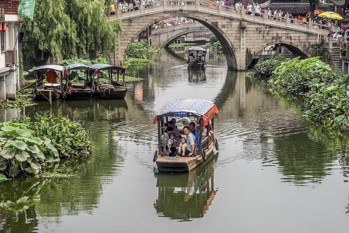 Sightseeing boat passing beneath a stone bridge in Qibao Ancient Town